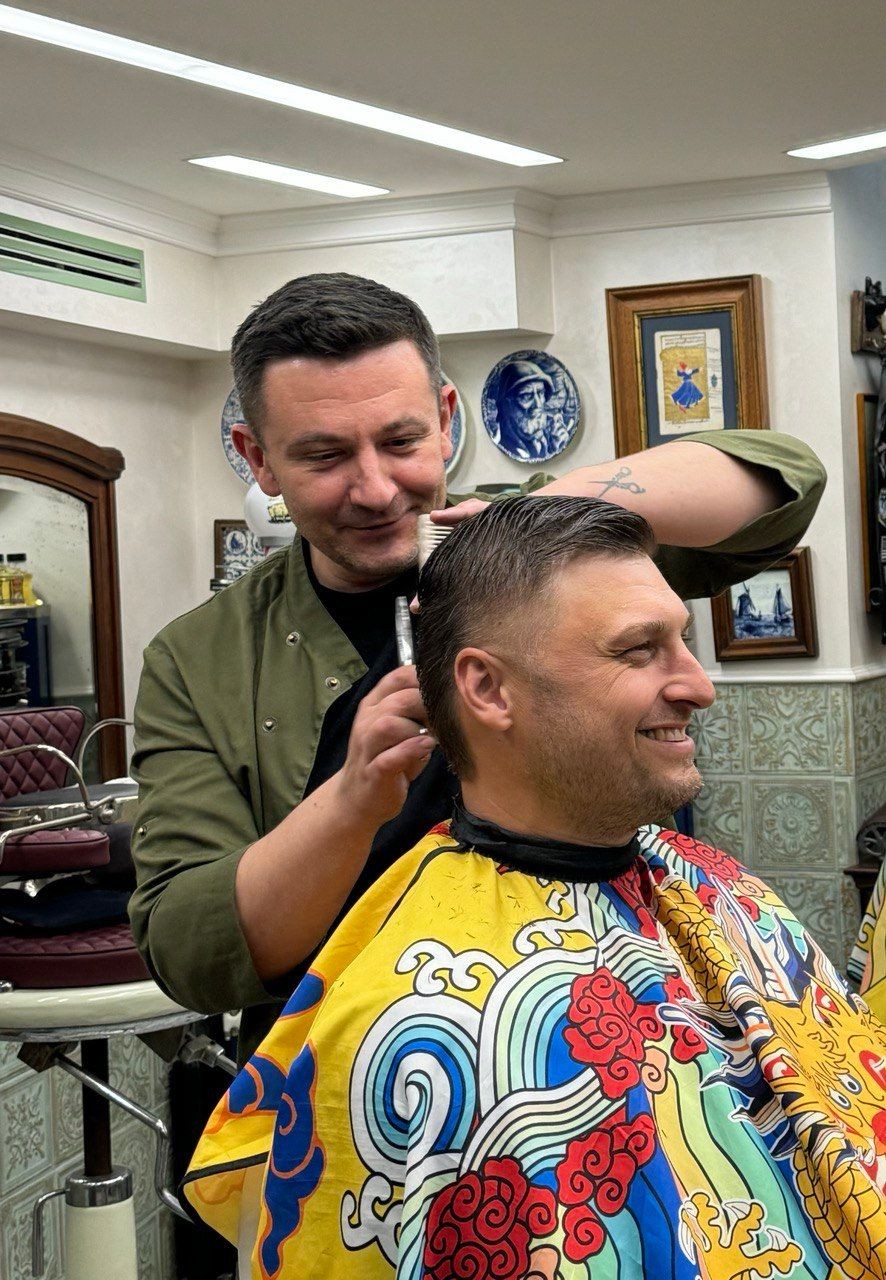 Barber styling a man's hair in a decorated salon, with colorful cape.