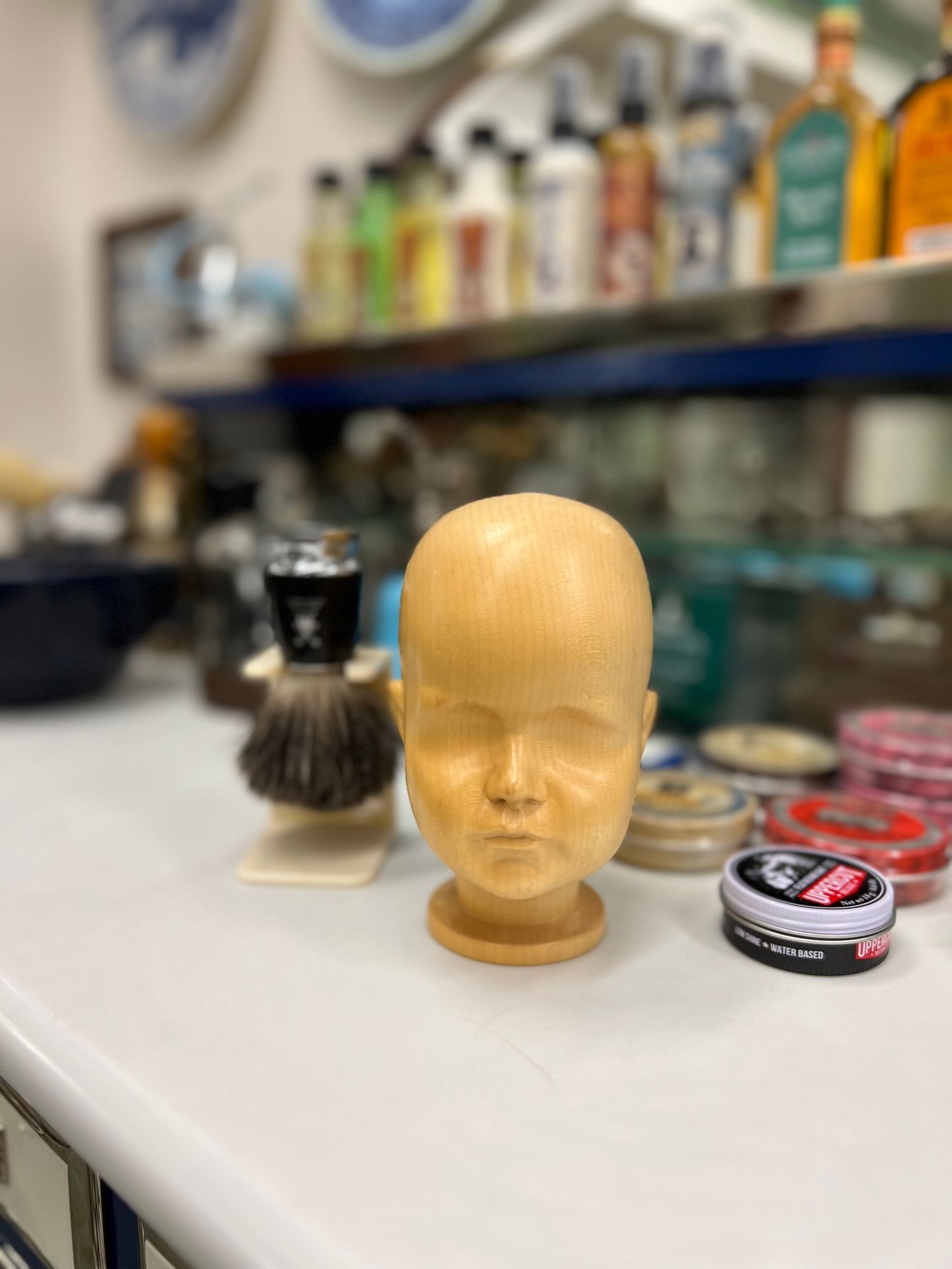 Wooden mannequin head on table with grooming products and shaving brush in barbershop.