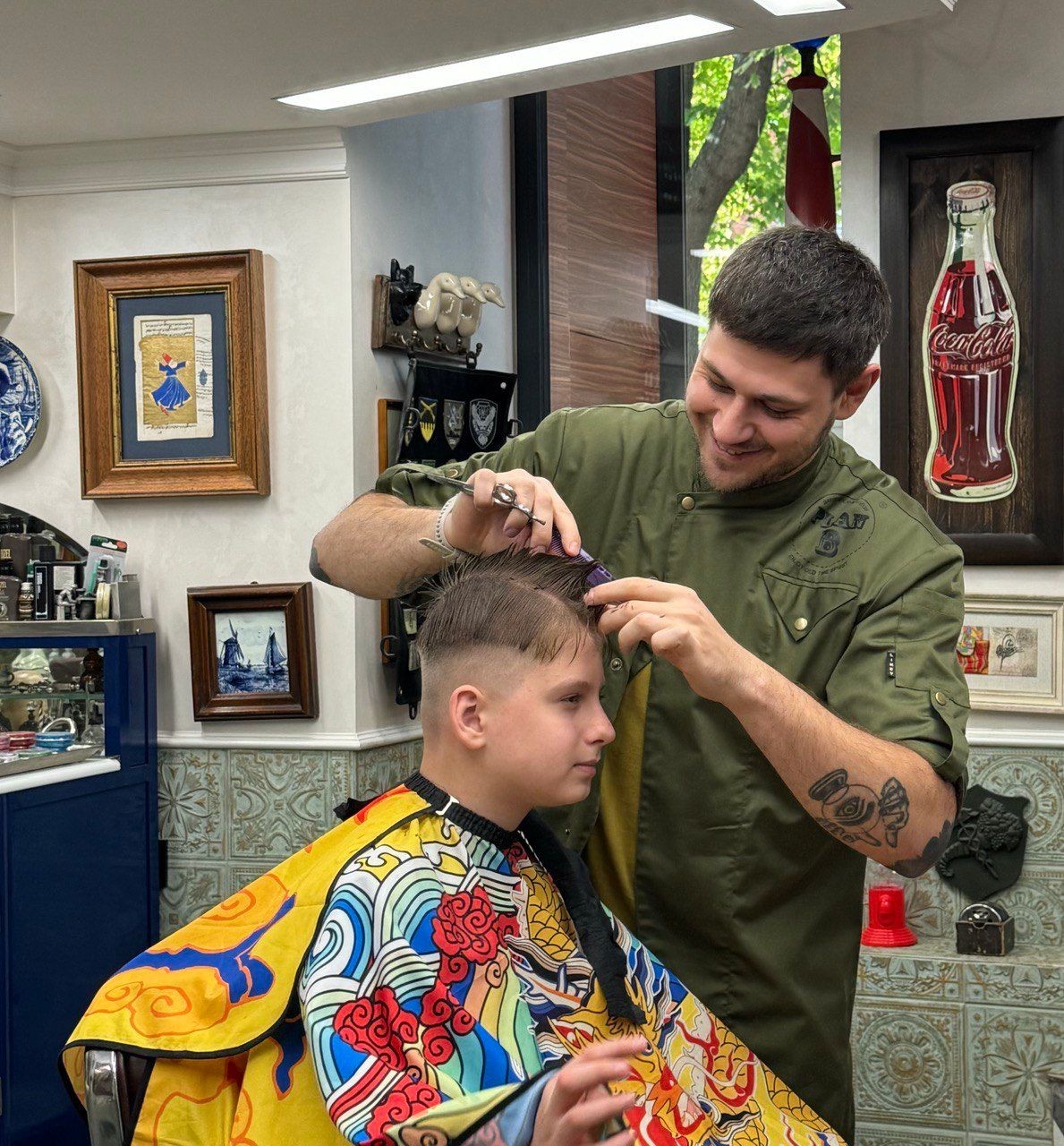Barber giving a young boy a haircut in a barber shop with colorful decor and framed artwork.