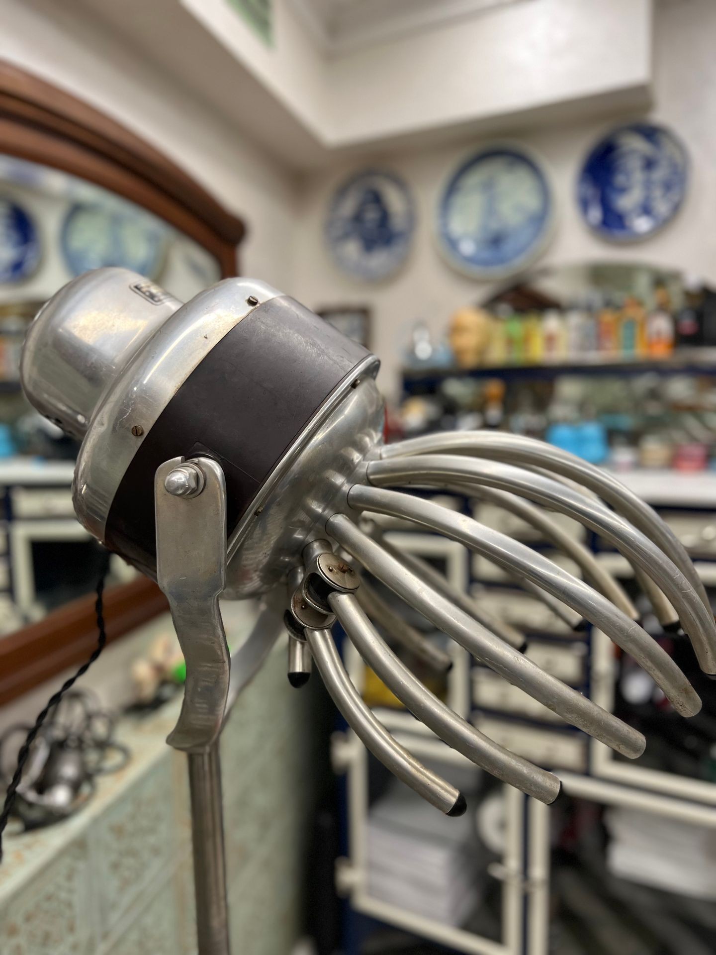 Close-up of a vintage metal hair dryer with multiple prongs in a barbershop setting.
