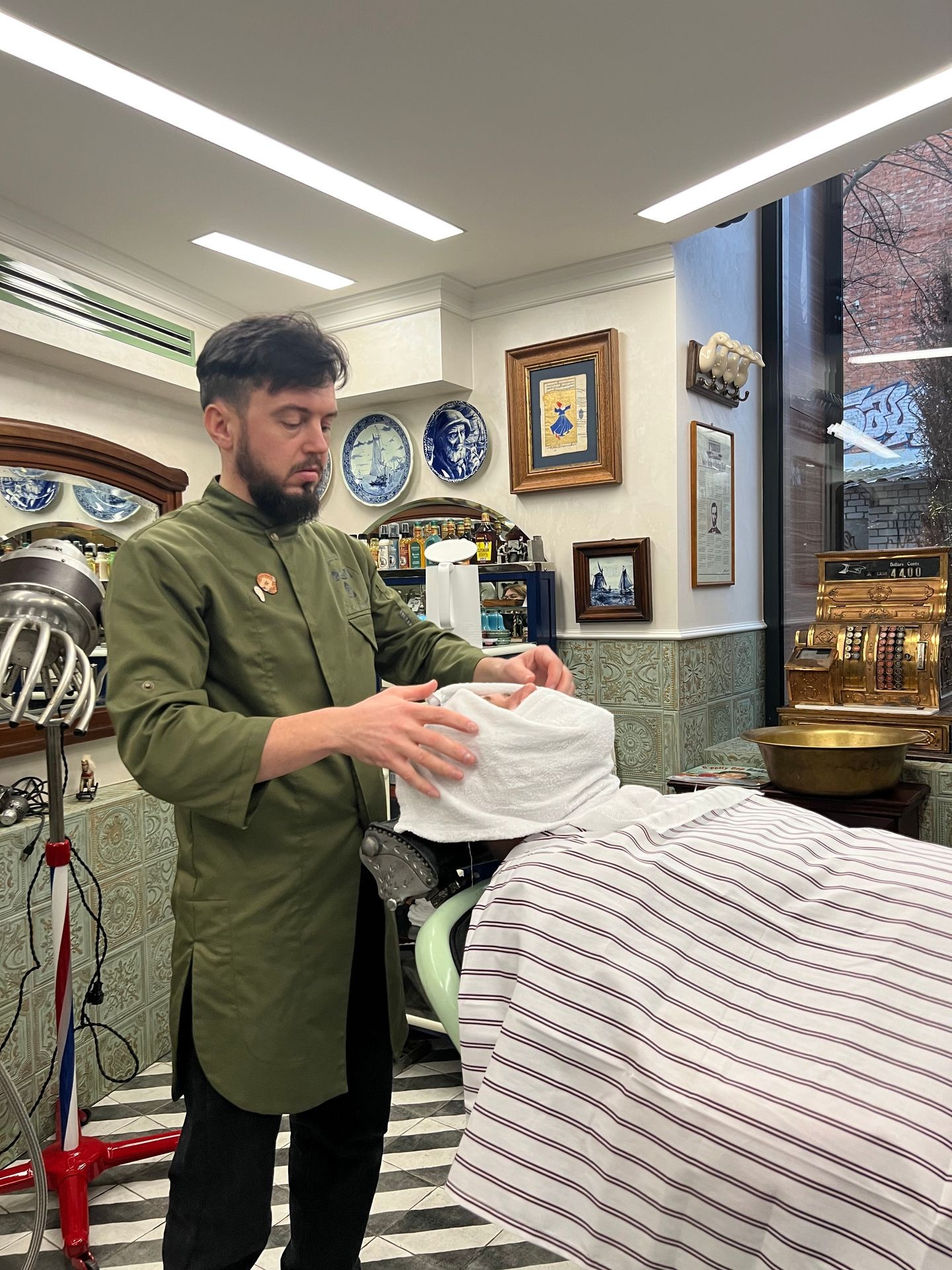 Barber applying a towel on a client's face in a vintage-style barbershop.